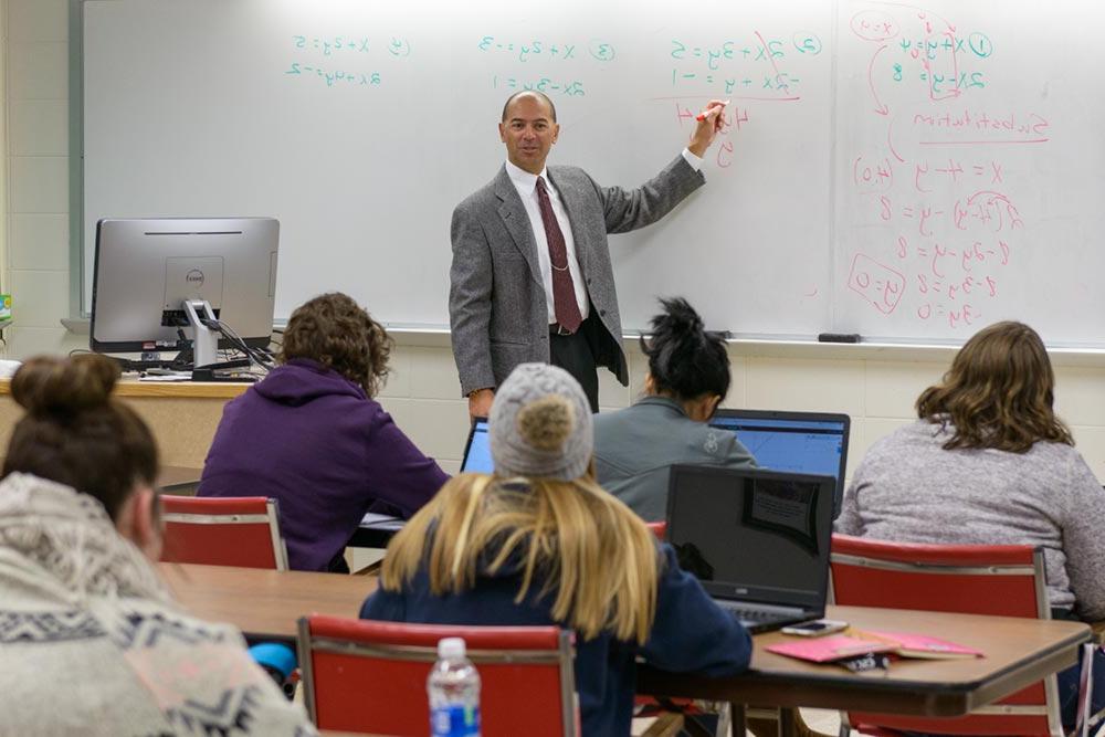 Math classroom scene with professor gesturing at equations on the whiteboard